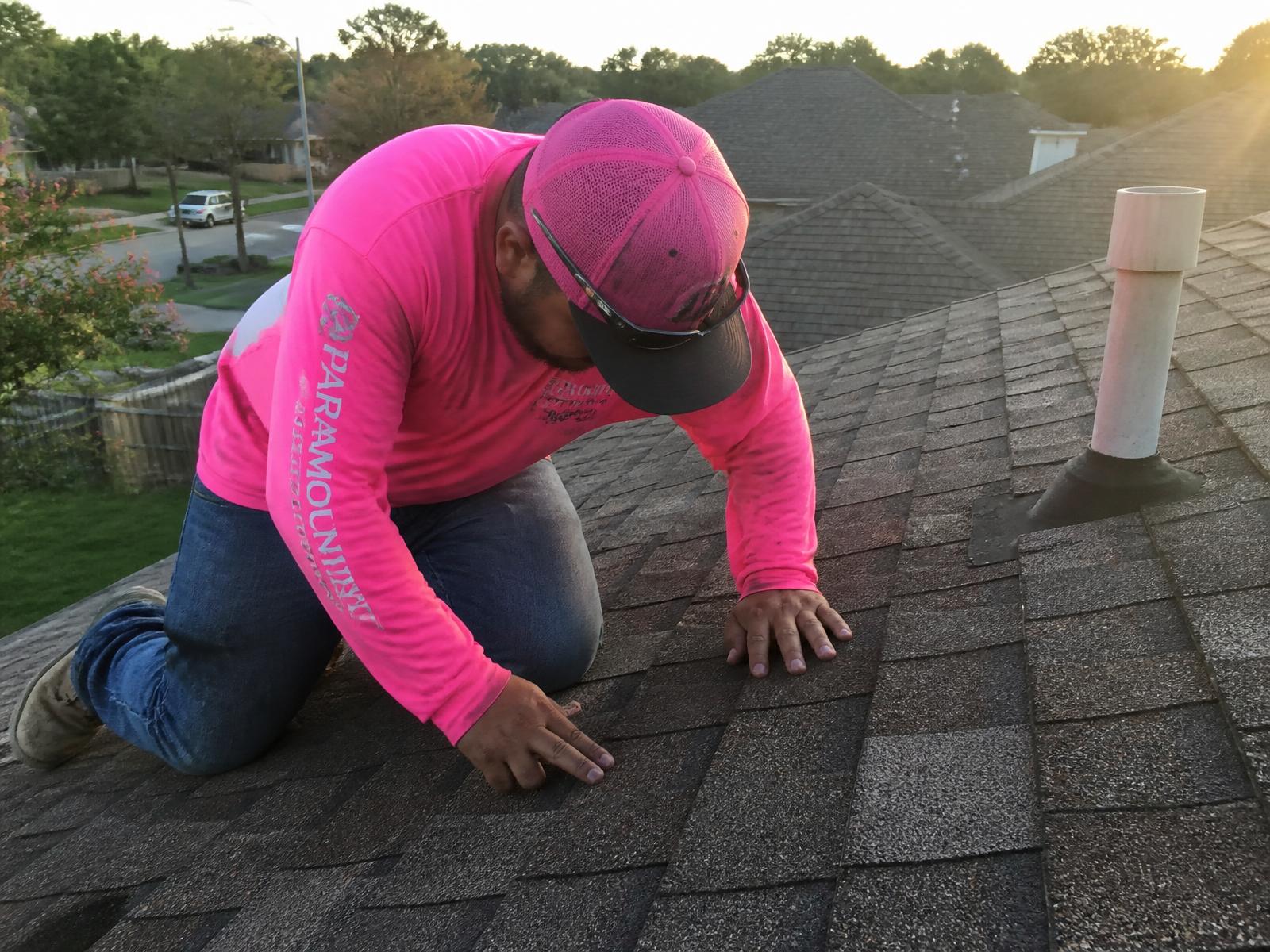 Trabajador de Taboras Roofing con camisa rosa inspeccionando las tejas de un techo residencial en Houston
